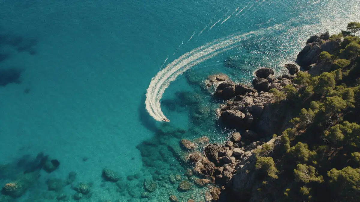 Vue aérienne d'une eau turquoise, rochers sombres et sillage d'un bateau.